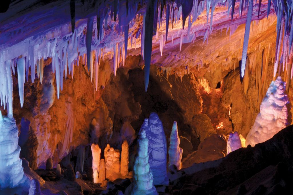 천장에 다양한 종유석이 매달려 있는 동굴과 땅에서 솟아오른 석순, 형형색색의 불빛이 비추는 석순.