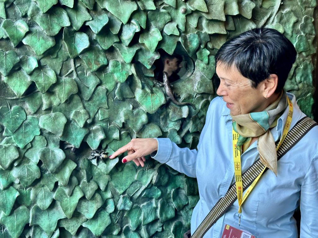 인공 녹색 잎으로 덮인 벽에 자리 잡은 작은 박쥐를 가리키는 사람. 그 사람은 웃으며 방아끈을 매고 있습니다.