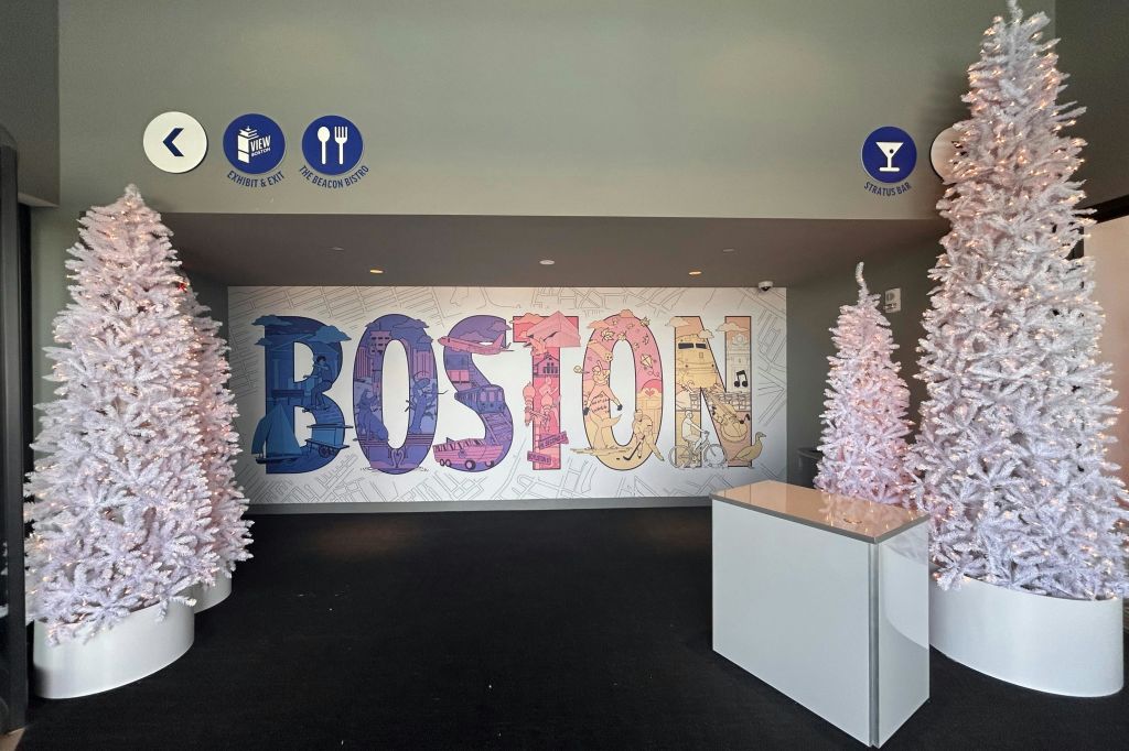 현대적인 실내 공간에 흰색 장식 나무 두 그루와 평범한 흰색 카운터가 있는 벽면에 화려한 "보스턴" 벽화가 있습니다.