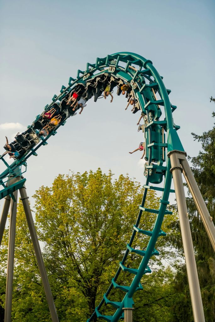 푸른 나무와 맑은 하늘을 배경으로 청록색 트랙이 달린 롤러코스터를 타는 사람들.