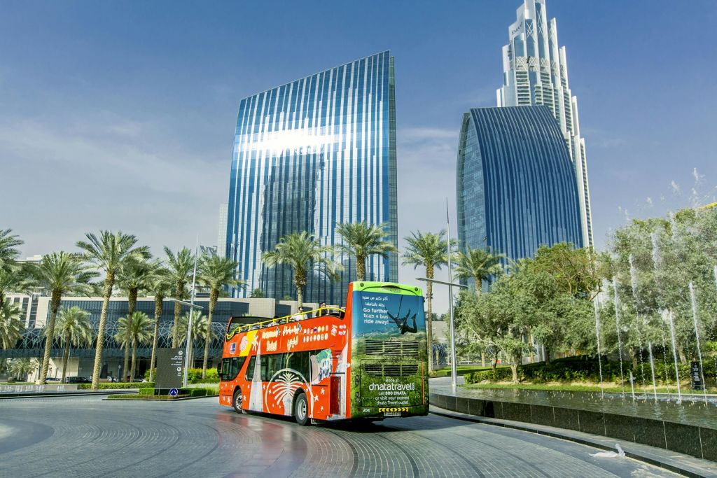 빨간색 2층 투어 버스가 야자수와 현대적인 고층 건물을 지나며 반사 유리 외관을 자랑합니다.