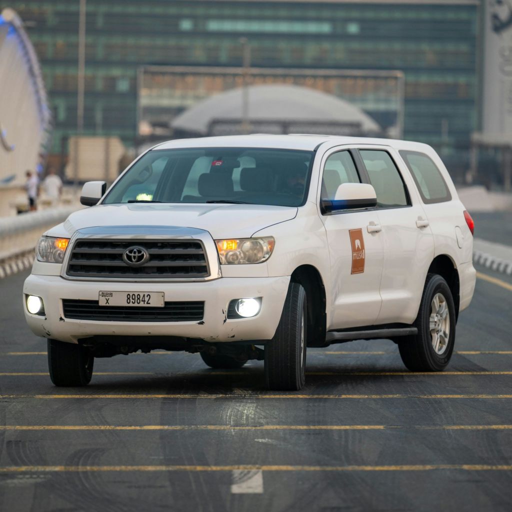 건물이 배경으로 보이는 도시 도로에서 주행하는 번호판 "89842" 가 있는 흰색 도요타 SUV입니다.