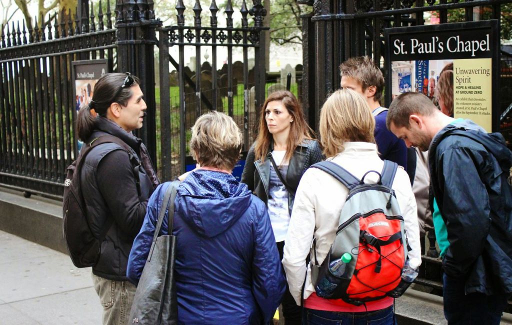 한 무리의 사람들이 철제 문 앞에 서 있으며, 배경에는 성 바울 성당 표지판이 보입니다.