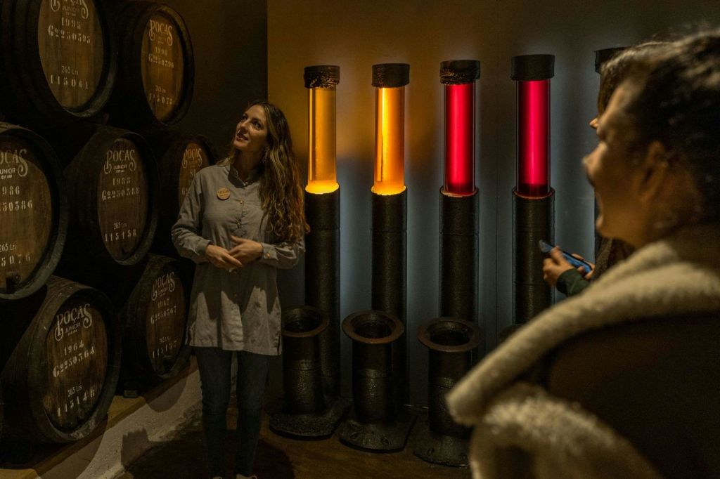 한 여성이 조명된 다채로운 튜브 앞에 서서 전시물이나 디스플레이로 보이는 통 옆에 서 있습니다.