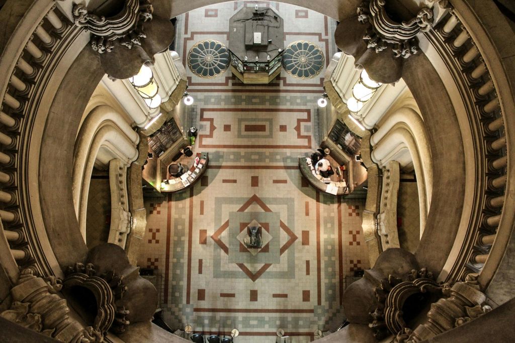 무늬가 있는 바닥, 두 개의 책상, 책으로 작업하는 사람들을 보여주는 높은 각도에서 건축 인테리어를 화려하게 꾸며보세요.