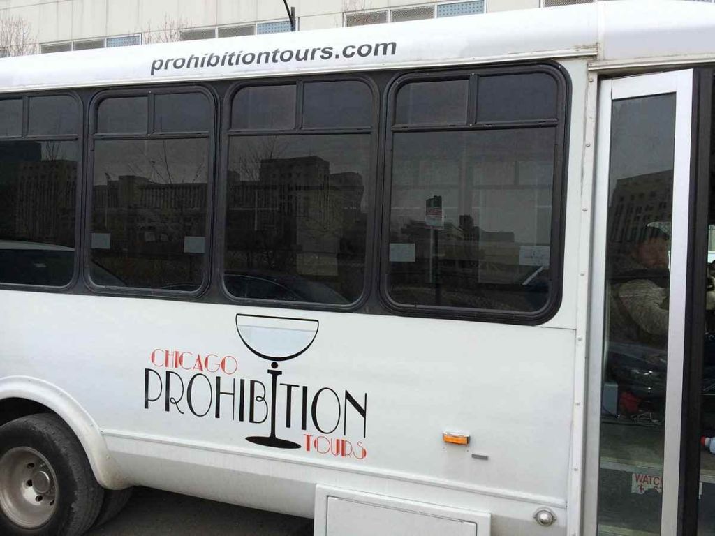측면과 창문 위에 "Chicago Prohibition Tours" 로고와 웹사이트 "prohibitiontours.com" 이 있는 흰색 버스.