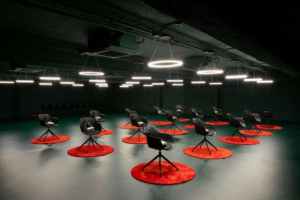 빨간색 원형 러그 위에 검은색 의자가 놓여 있고 반지 모양의 천장 조명으로 조명이 켜진 어두운 조명 객실입니다.