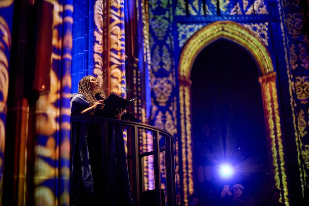 한 사람이 화려하고 빛나는 대성당 내부 앞 플랫폼에 서서 책을 들고 위를 바라보고 있습니다.