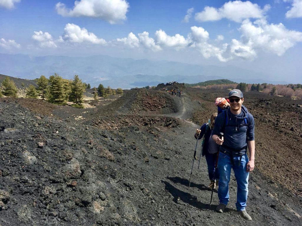등산로가 있는 바위길에서 하이킹을 즐기는 사람들, 부분적으로 흐린 하늘 아래 흩어져 있는 나무와 산을 배경으로 하이킹을 즐기는 사람들.