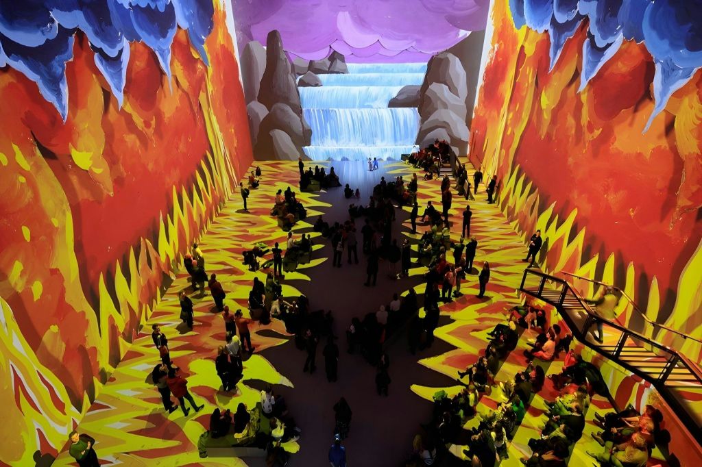 활기찬 폭포 풍경과 불타는 패턴이 투영된 넓은 실내 공간으로 많은 사람들이 앉아서 서 있습니다.