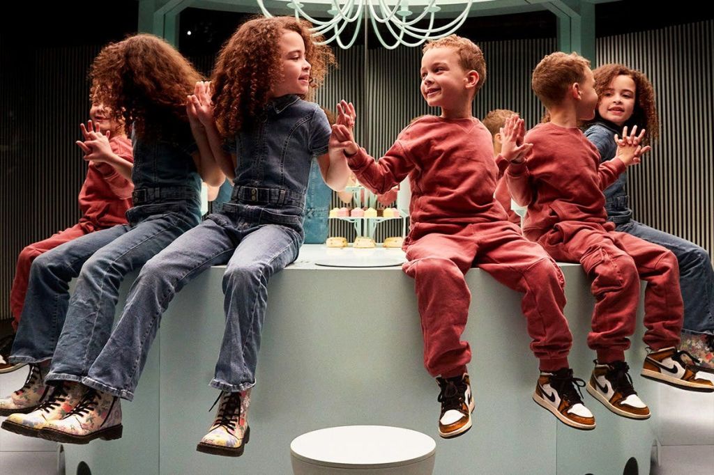 두 어린이가 현대적인 인테리어의 카운터에 앉아 미소를 짓고 손을 잡고 있으며, 거울은 그들의 모습을 반영하고 있습니다.