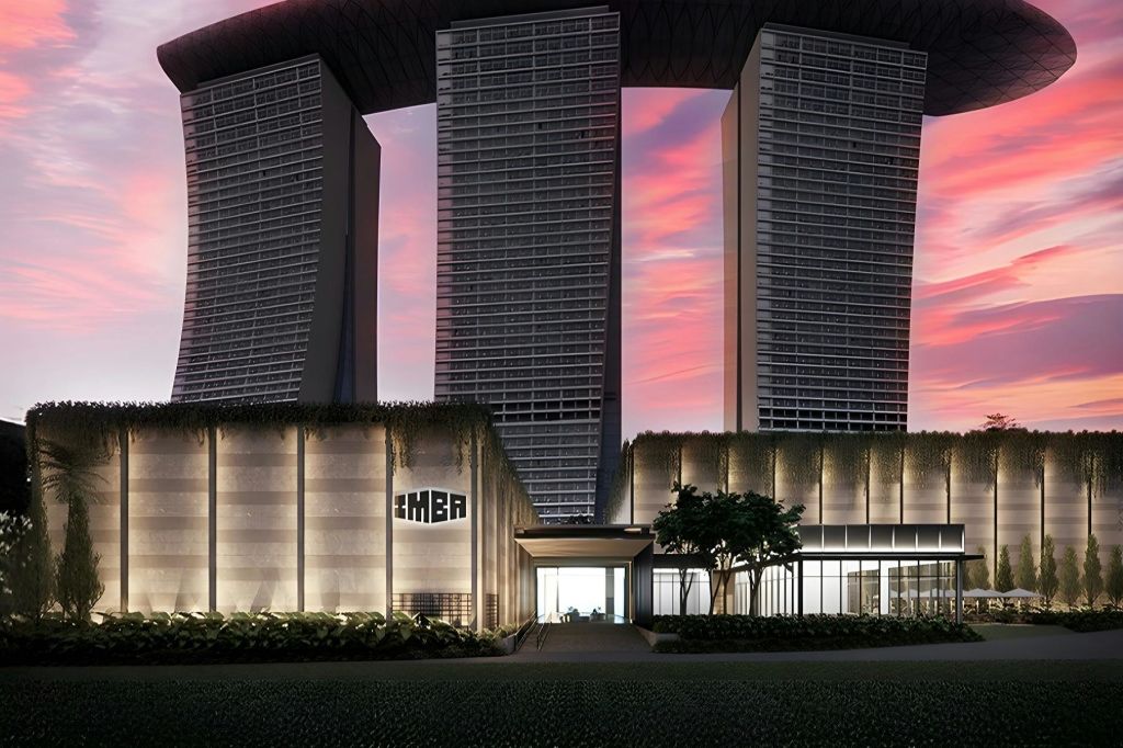 대형 유리 표면과 수직 외관을 갖춘 현대적인 건물로 분홍색과 보라색 석양 하늘을 배경으로 합니다.