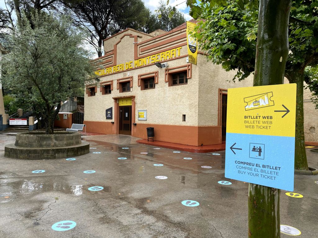 "Aeri de Montserrat" 라고 표시된 입구의 건물로, 티켓 구매 정보를 나타내는 표지판과 마커가 있습니다.