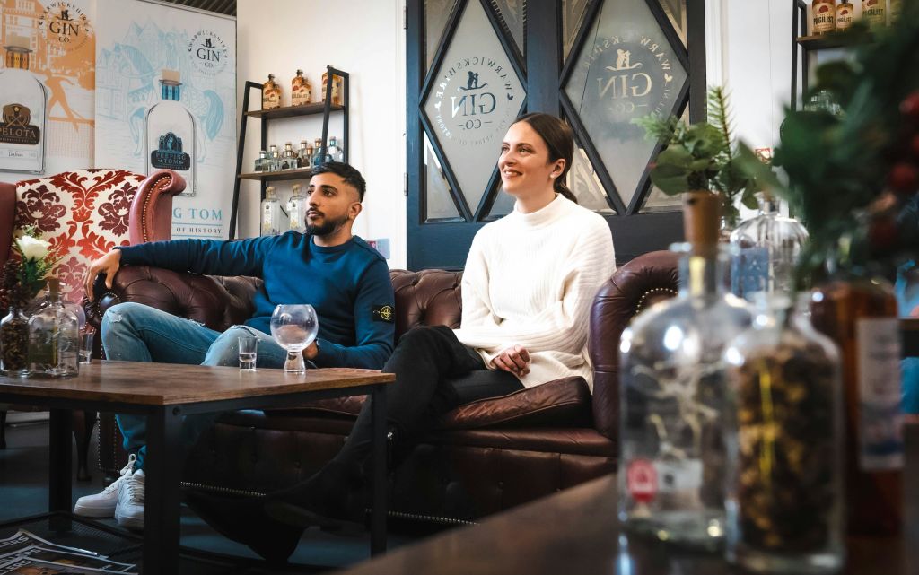 선반에 진병이 놓여 있고 장식용 유리문이 있는 아늑한 방의 가죽 소파에 한 남녀가 앉아 있습니다.