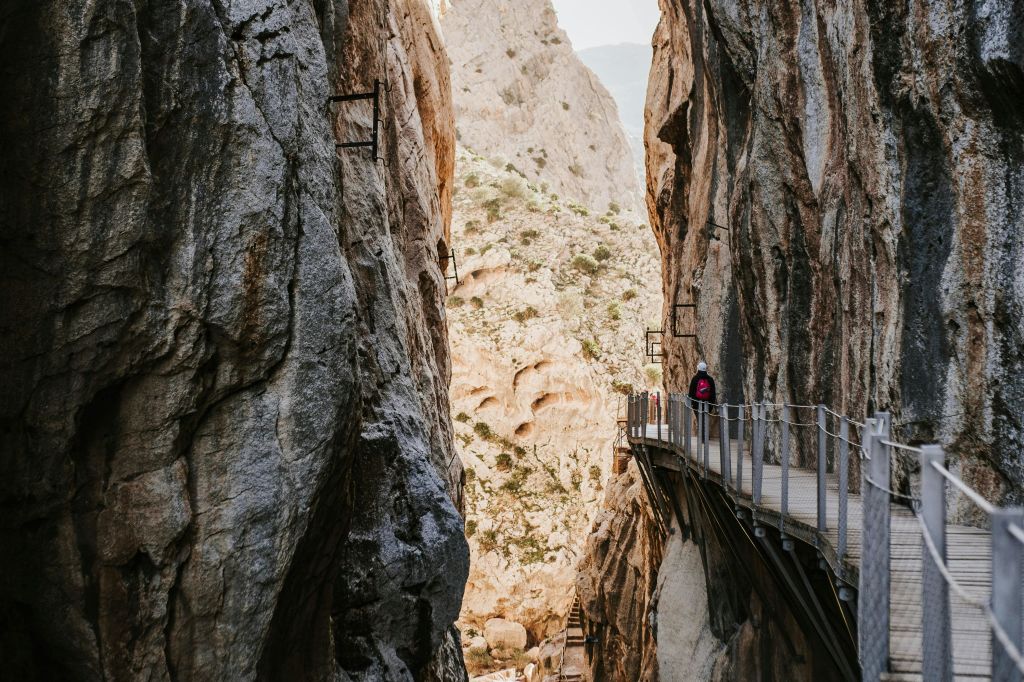 암벽에 통로가 붙어 있는 좁은 협곡, 그 위를 걷는 사람, 저 끝을 비추는 햇빛.