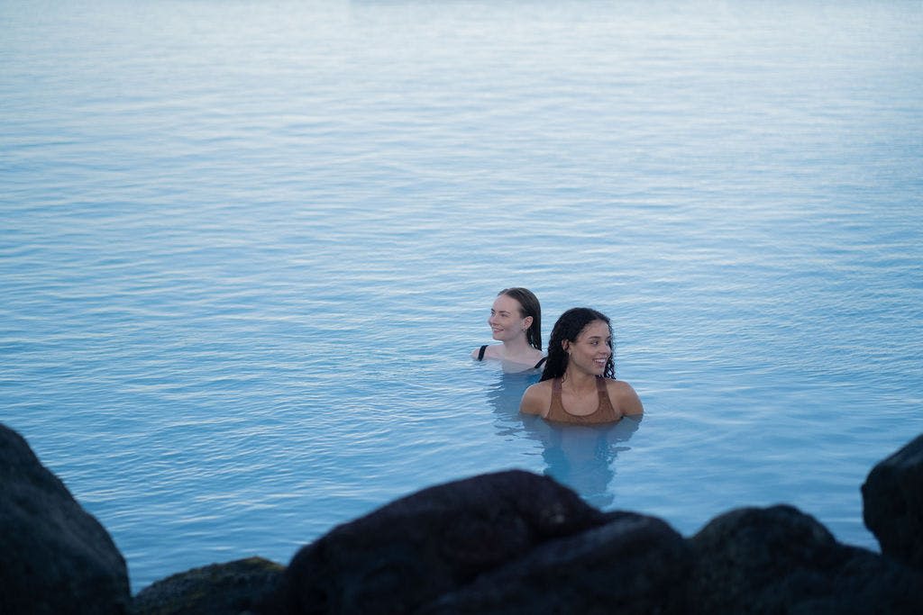 전경에 어두운 바위가 있는 잔잔하고 푸른 물 속의 두 사람.