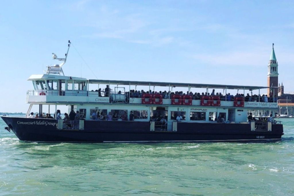 승객으로 가득 찬 페리가 맑고 푸른 하늘 아래 잔잔한 물줄기를 타고 항해하고 있습니다.