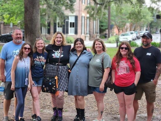 건물과 나무를 배경으로 공원을 배경으로 여섯 명이 서서 미소를 짓고 있습니다.