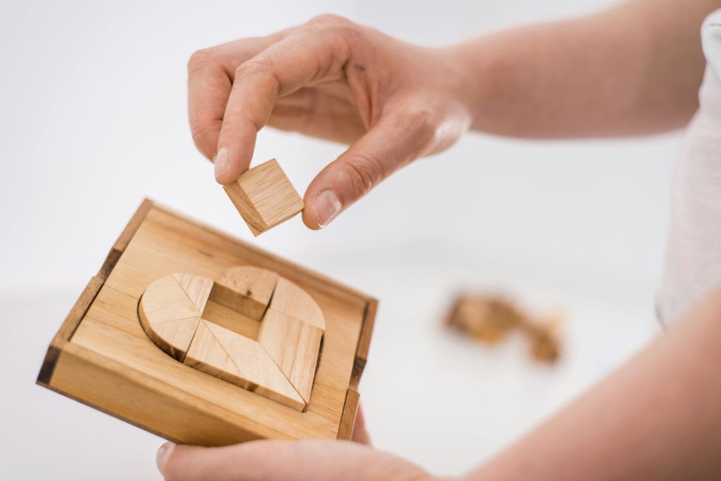 하트 모양의 조각이 있는 나무 퍼즐을 잡고 사각형 조각을 퍼즐에 넣습니다.