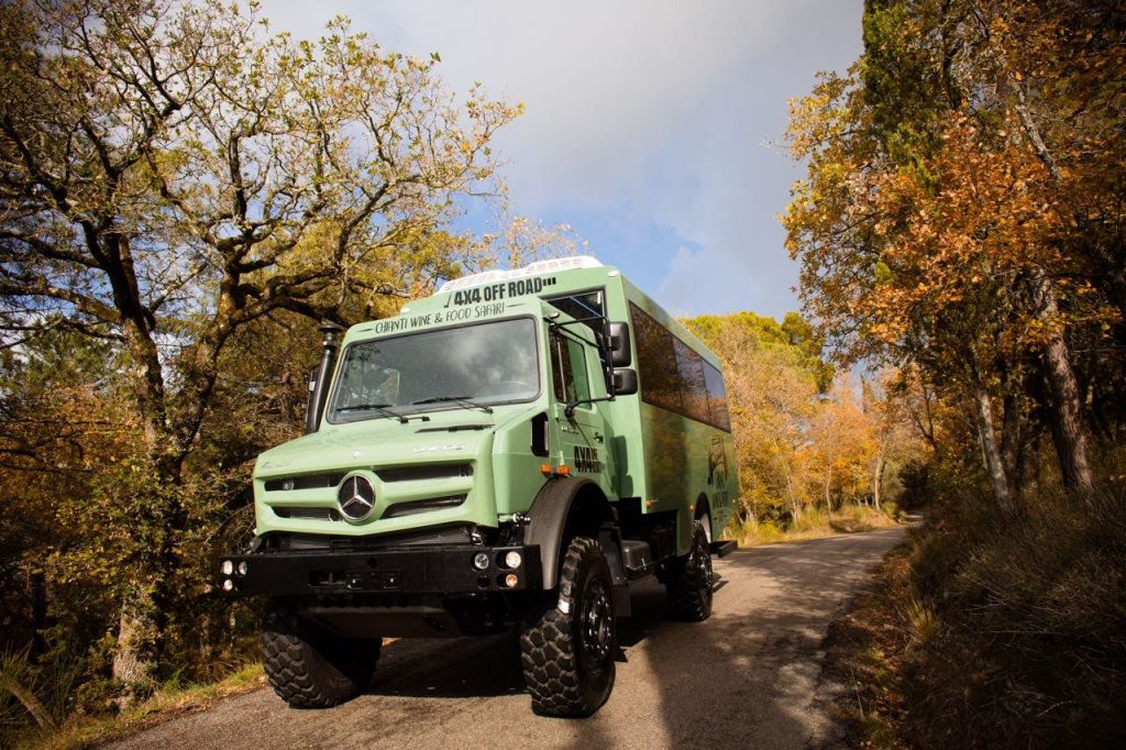 가을 나무로 둘러싸인 좁은 도로에 녹색 메르세데스 4x4 오프로드 차량이 주차되어 있습니다.
