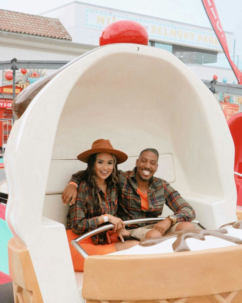 격자무늬 셔츠를 입은 미소 짓는 커플이 조개껍질 모양의 테마파크 놀이기구에 앉아 있습니다.