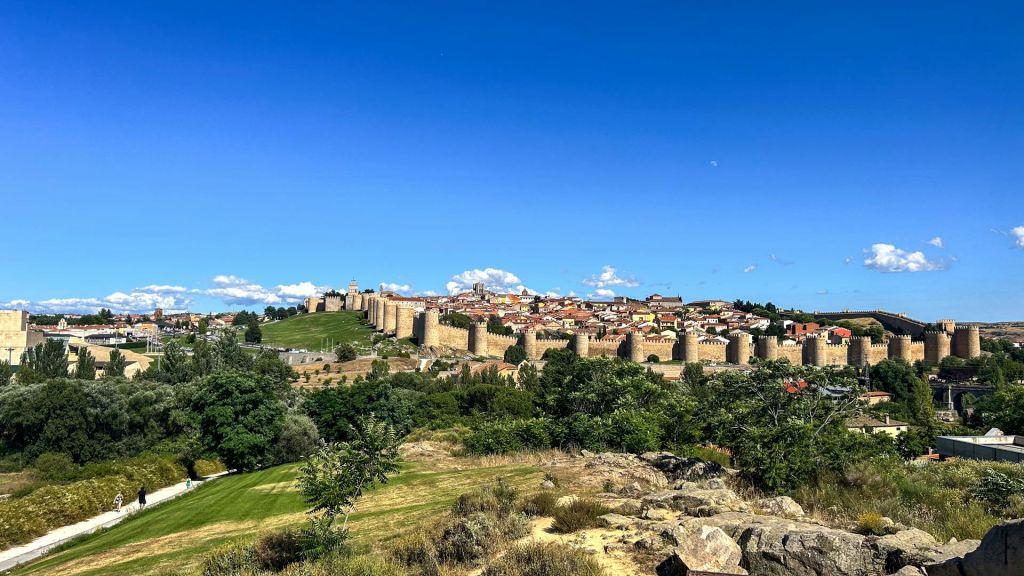 맑고 푸른 하늘 아래 녹음으로 둘러싸인 돌담과 탑이 있는 중세 도시.