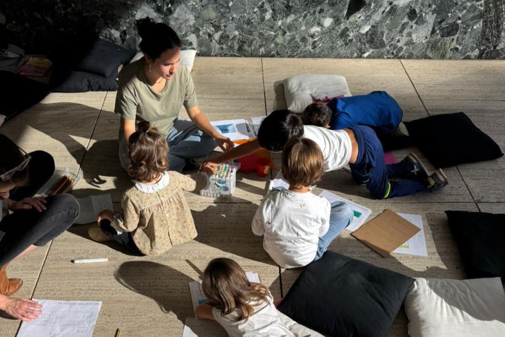 한 여성이 어린 아이들로 둘러싸인 바닥에 앉아 종이와 미술 용품으로 활동하고 있습니다.
