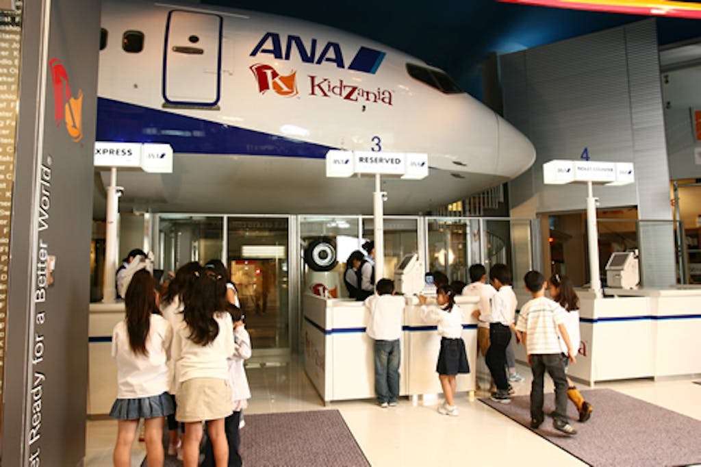 키자니아 내부의 ANA 비행기가 있는 시뮬레이션 공항 체크인 구역에 줄을 서 있는 어린이.