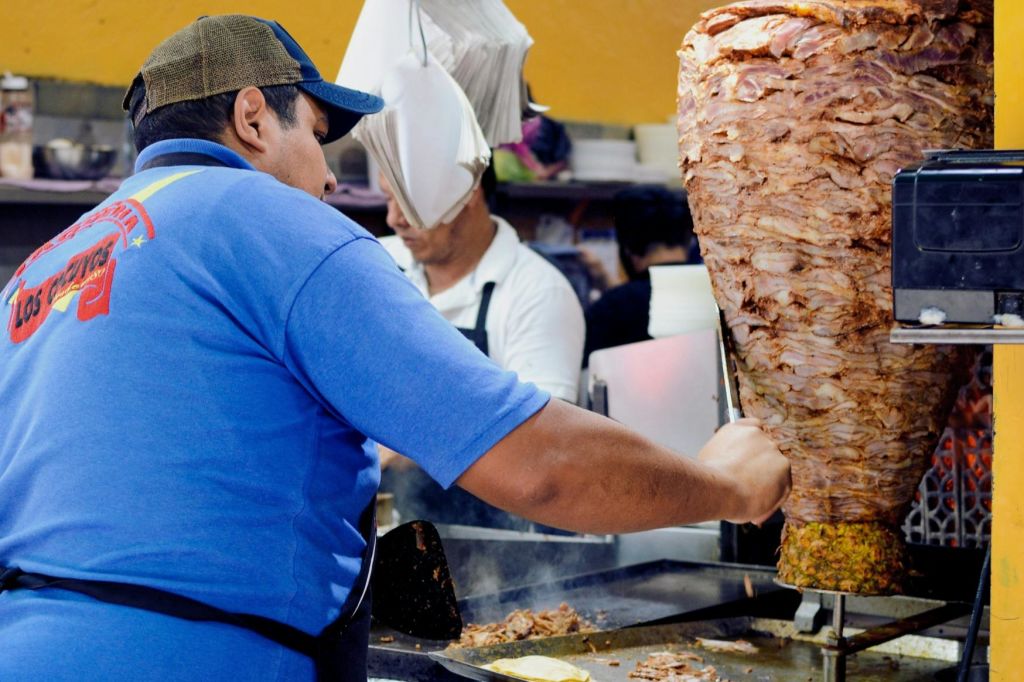 타케로는 북적거리는 타케리아에서 양념된 돼지고기를 수직 침으로 전문적으로 조각합니다.