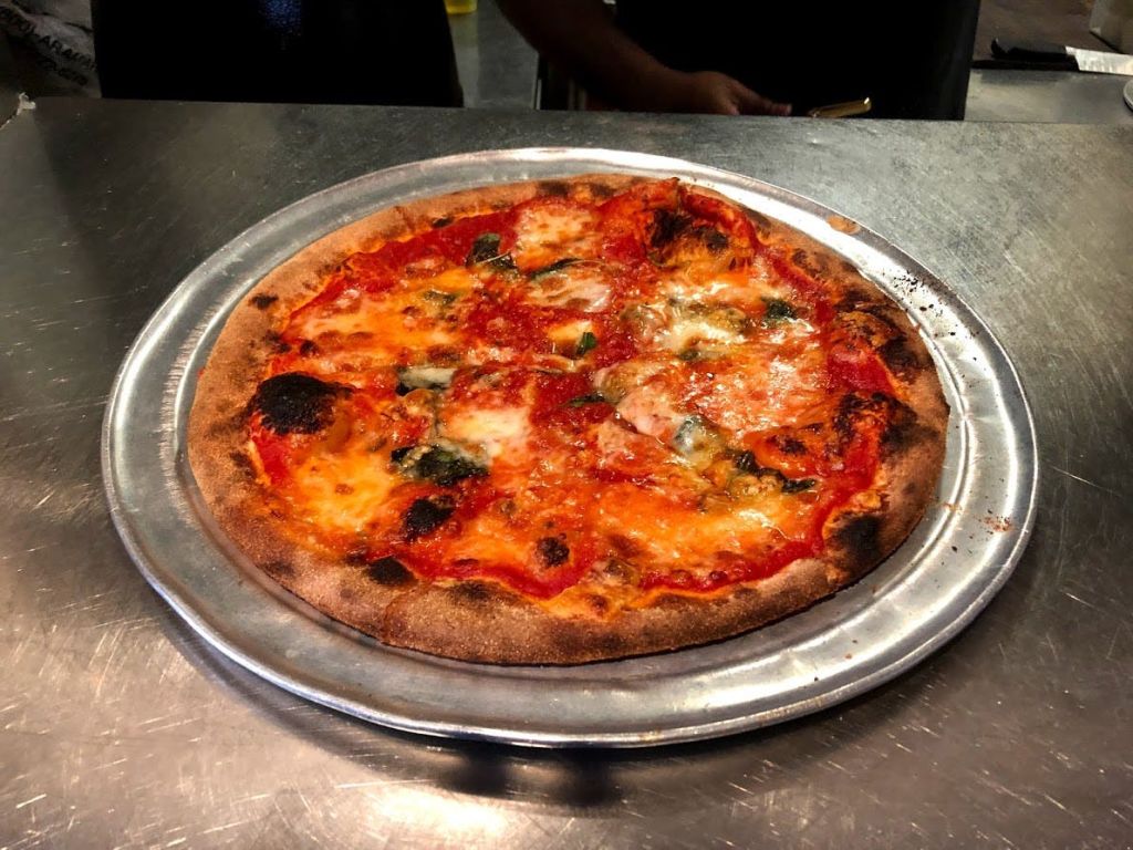 금속 트레이에 조리된 마르게리타 피자, 눈에 띄게 모서리가 돌진하고 조리대에 녹은 치즈가 있습니다.