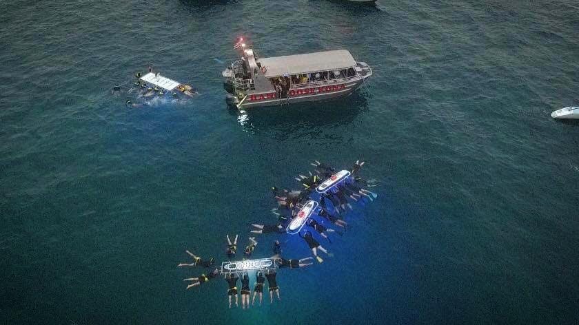 야간에 조명이 켜진 뗏목과 어두운 물 위 보트 근처에서 단체로 수영하는 사람들.