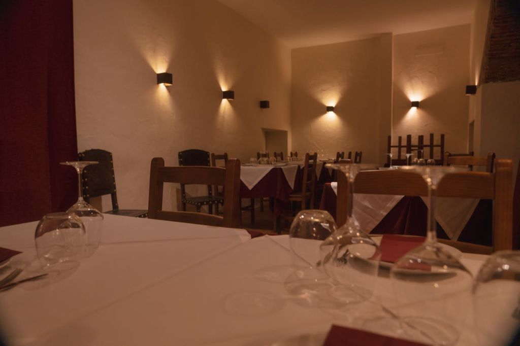 나무 의자, 흰색 식탁보, 와인잔, 벽걸이 조명이 있는 조명이 희미하고 우아한 레스토랑입니다.