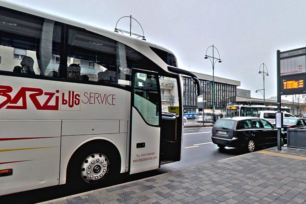 '버스 서비스' 라고 표시된 흰색 버스가 건물과 차량을 배경으로 보도 옆의 도시 거리에 주차되어 있습니다.