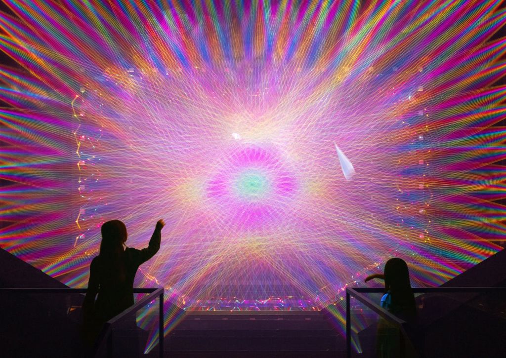 두 개의 실루엣 피규어가 동심원 패턴을 투영하는 생동감 넘치는 멀티컬러 라이트 디스플레이와 상호 작용합니다.