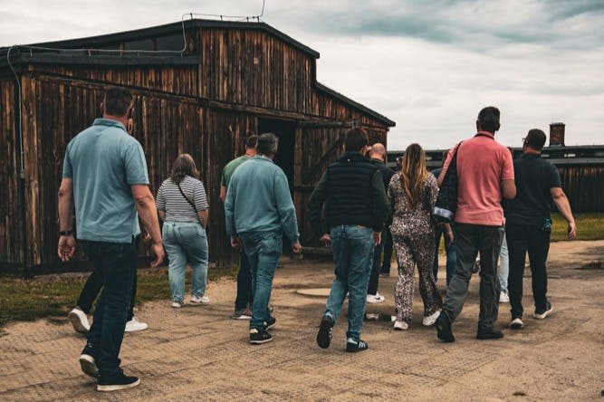 흐린 날 풍화된 목조 건물을 향해 걸어가는 한 무리의 사람들.