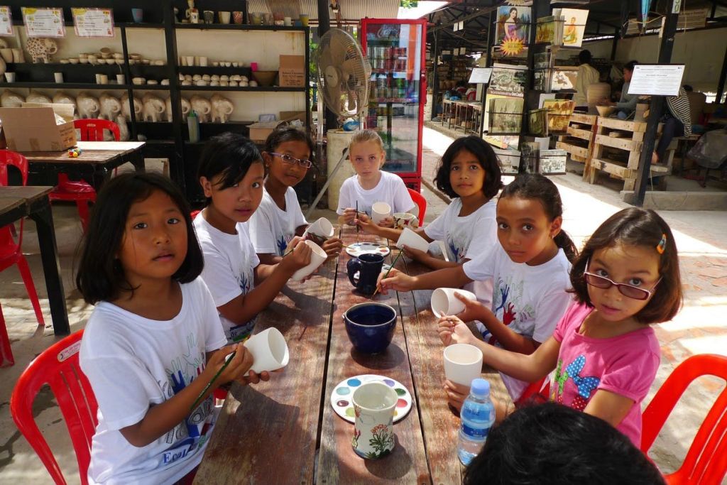 테이블에 앉아 도자기 소품이 가득한 아트 스튜디오에서 다양한 페인트 색상의 세라믹 머그잔을 그리는 어린이들.