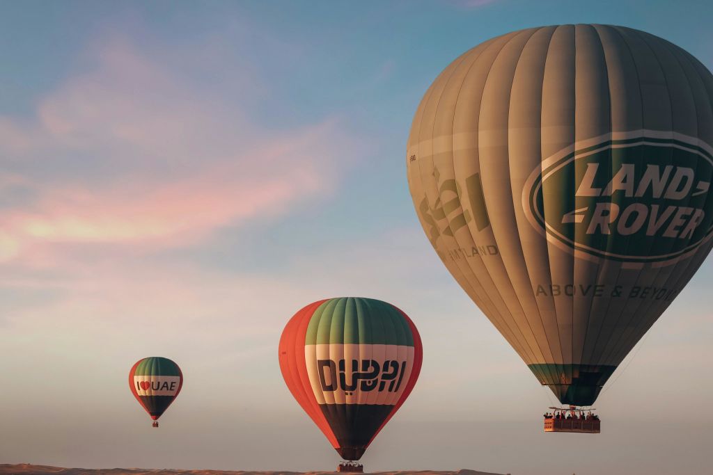 하늘에는 세 개의 열기구가 있는데, 하나는 '아랍에미리트', 다른 하나는 '두바이', 세 번째는 화려한 석양을 배경으로 한 로고가 있습니다.