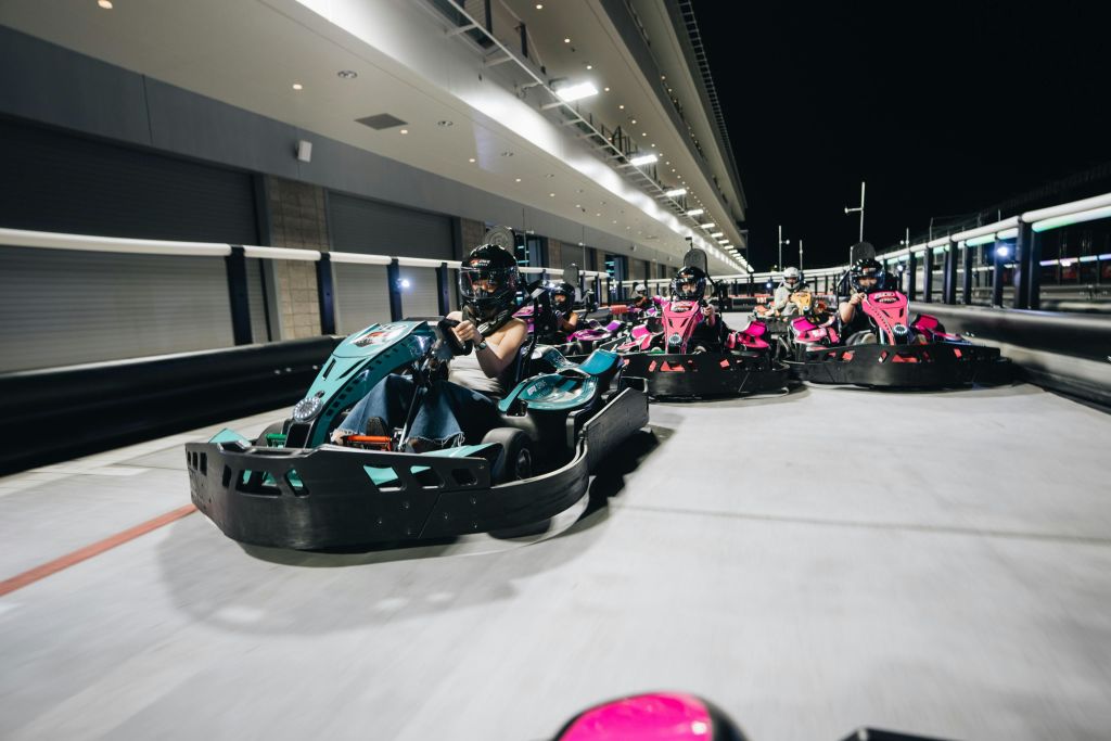 밝은 색상의 고카트를 타고 야간에 조명이 켜진 트랙을 달리는 사람들.