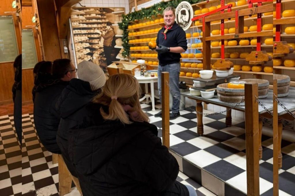 치즈 바퀴가 달린 선반과 체크무늬 바닥이 있는 상점에서 관객에게 치즈를 시연하는 사람.