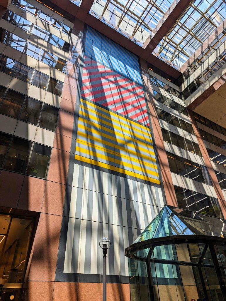 크고 화려한 추상 벽화, 유리 아트리움, 기하학적 채광창이 있는 현대식 건물의 내부.