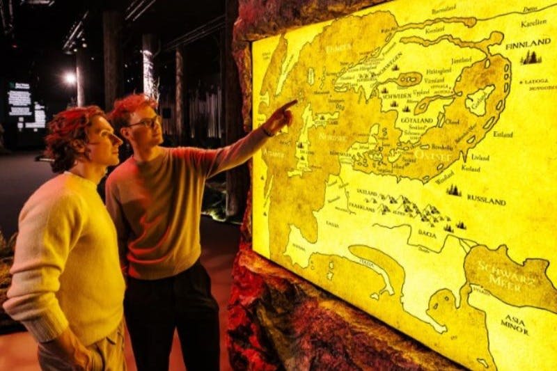 두 사람이 희미하게 빛나는 전시 공간에서 조명된 역사 지도를 살펴보고, 하나는 지도를 가리킵니다.