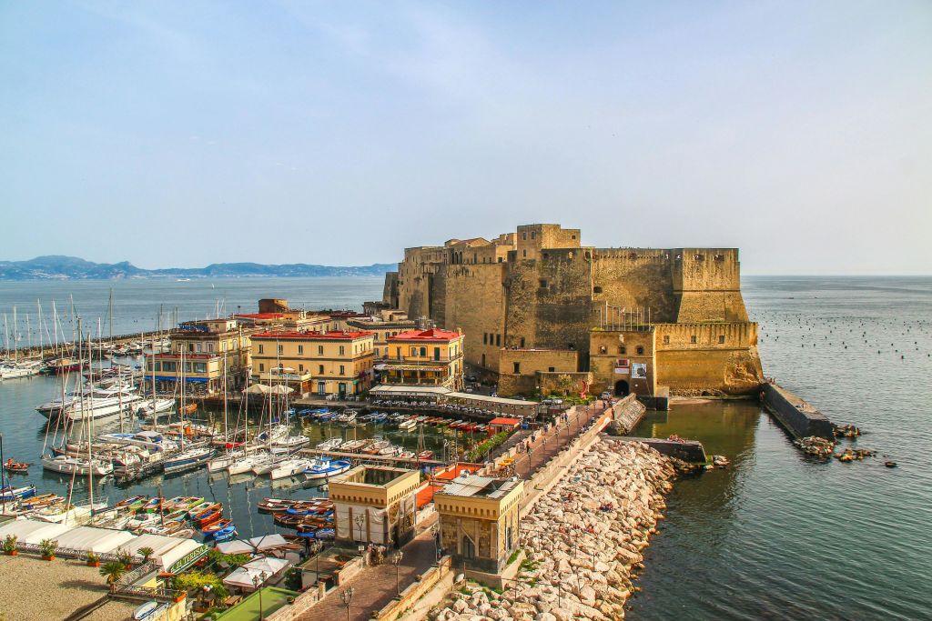 배가 가득한 정박지와 맑은 하늘 아래 근처 건물이 있는 바닷가의 유서 깊은 석조 요새입니다.