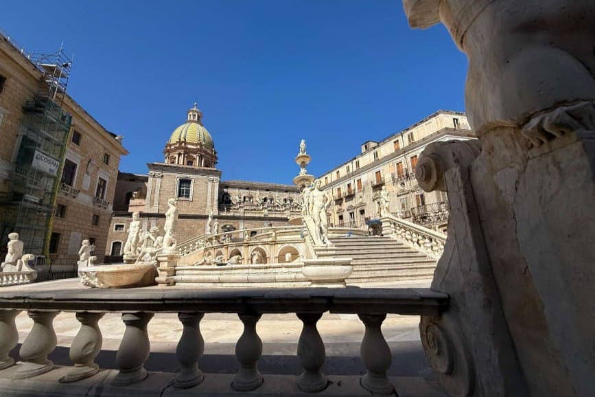 돔형 건물, 화려한 계단, 맑고 푸른 하늘 아래 조각상이 있는 유서 깊은 광장입니다.