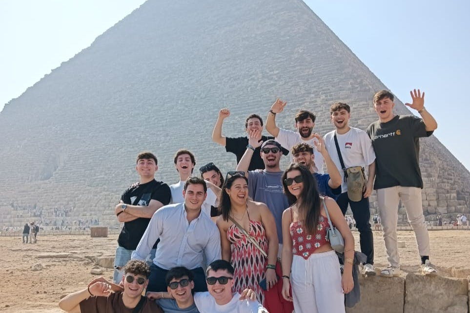 한 무리의 사람들이 맑고 푸른 하늘 아래 피라미드 앞에서 미소를 짓고 포즈를 취하고 있습니다.