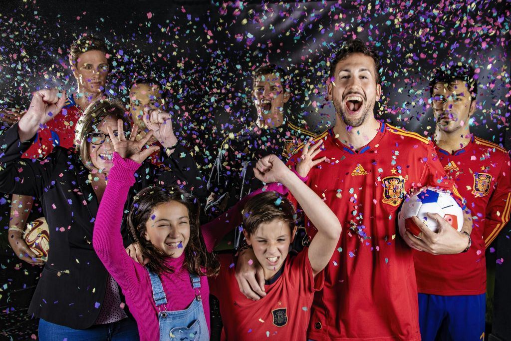 떨어지는 색종이 아래에서 축하하고 웃으며 응원하는 사람들의 그룹. 일부는 빨간색 스포츠 유니폼을 입습니다. 분홍색 스웨터를 입은 어린이가 미소를 짓고 있습니다.