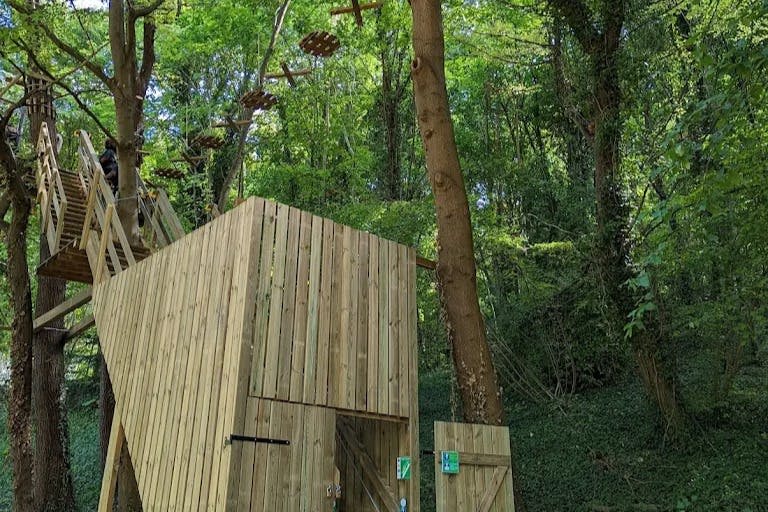 울창한 푸른 숲의 목조 건축물과 등반 플랫폼, 나무 사이로 펼쳐지는 로프 어드벤처 코스.