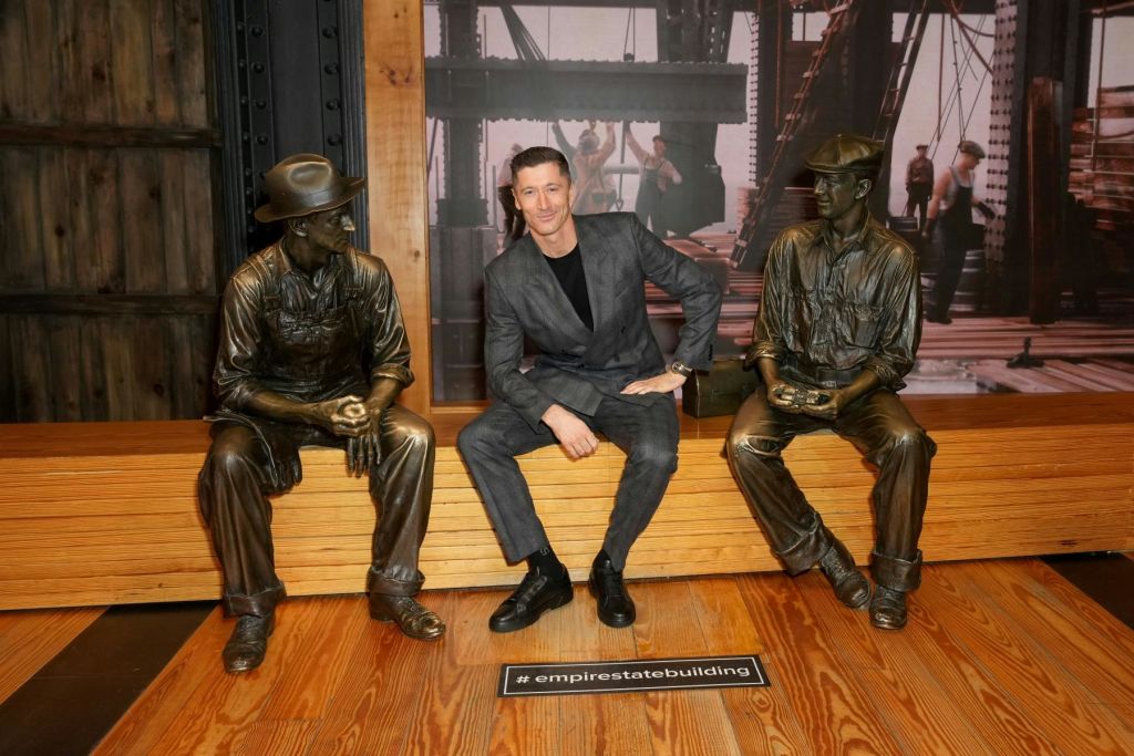 건물 내부의 두 개의 청동 조각상 사이에 앉은 사람으로, 건설 노동자를 배경으로 하고 있습니다. '# empirestatebuilding' 이라는 표지판이 있습니다.