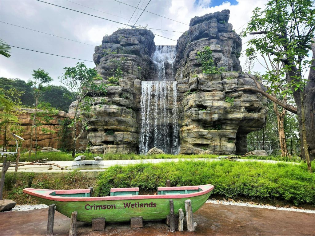 폭포와 녹지가 있는 커다란 바위 지층 앞에 "홍색 습지" 라고 표시된 초록색과 빨간색 보트가 있습니다.