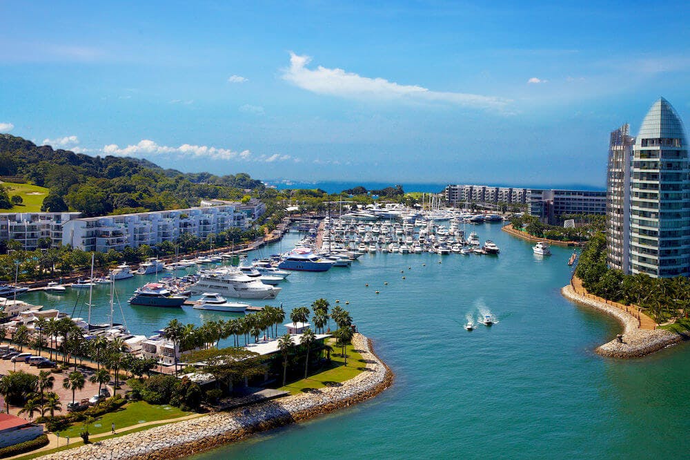 맑고 푸른 하늘 아래 건물과 녹지, 잔잔한 바다로 둘러싸인 수많은 선착장 보트가 있는 정박지입니다.