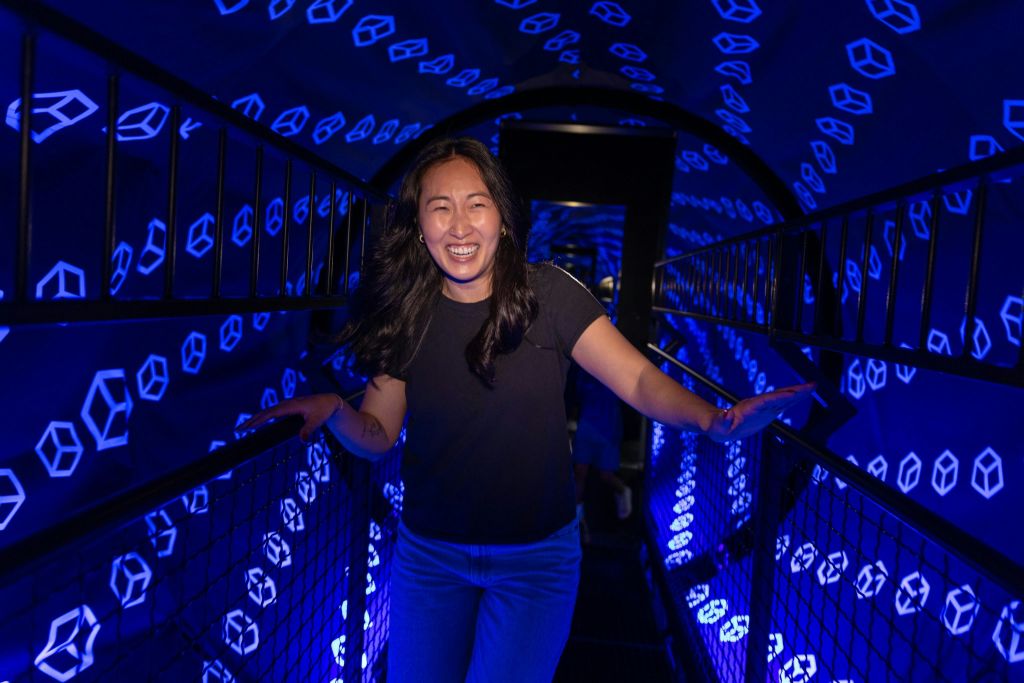 한 사람이 파란색 기하학적 모양의 벽이 터널처럼 보이는 통로에 서서 미소를 짓고 있습니다.